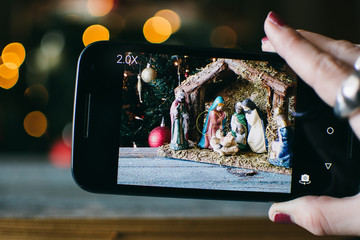 person takes photo of Christmas Manger scene with figurines including Jesus, Mary, Joseph, sheep and magi.