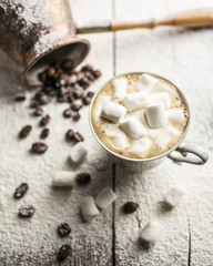 Hot black coffee in a cup with marshmallows and grains beside cuzve is located on the old a wooden table sprinkle with powdered sugar