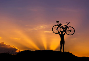 Fototapeta na wymiar Silhouette the man stand in action lifting bicycle above his head on the meadow on sunset