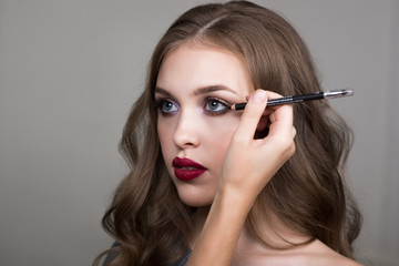 Make-up process, the face of a beautiful young woman and makeup artist's hand with a pencil for eyes. Cropped image
