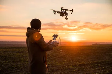 Foto op Plexiglas Man operating a drone with remote control. Dark silhouette against colorful sunset. Soft focus. © dianagrytsku