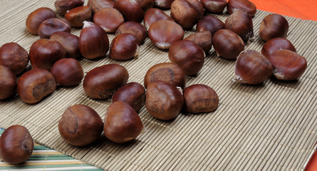 raw chestnuts on bamboo napkin over orange wooden background