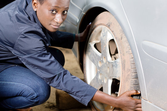 Young woman mechanic squatting near a car removes her tire. - Powered by Adobe