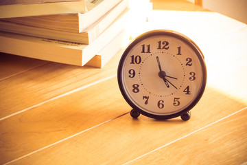 Clock on a table with blurry books background vintage tone style 