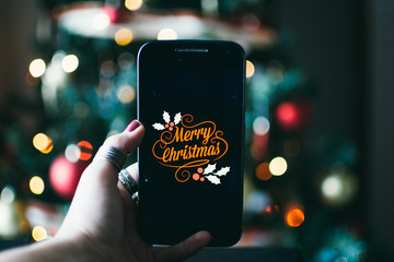 person takes a photo on a smartphone of merry christmas with a christmas background