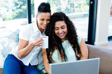 Happy lesbian couple having coffee and using laptop