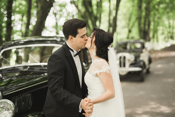 Happy newlywed couple, man and wife kissing near stylish retro car