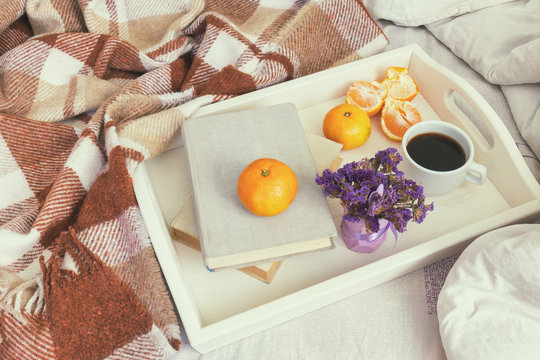 Breakfast in bed. Old book, tangerines and cup of coffee in tray, cozy home concept. Coloring and processing photo with soft focus.