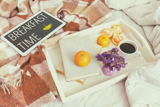 Breakfast in bed. Old book, tangerines and cup of coffee in tray, tablet with breakfast time concept, cozy home concept. Coloring and processing photo with soft focus.