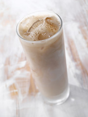 Gold drink with ice. Photographed on a light wooden background. Light illumination.