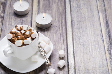 Fototapeta na wymiar Hot chocolate with marshmallow in white cup and two candles on wooden table. Copy space