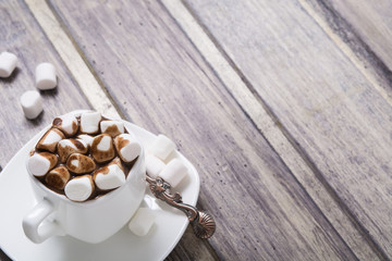 Hot chocolate in white cup with marshmallow on wooden table. Copy space
