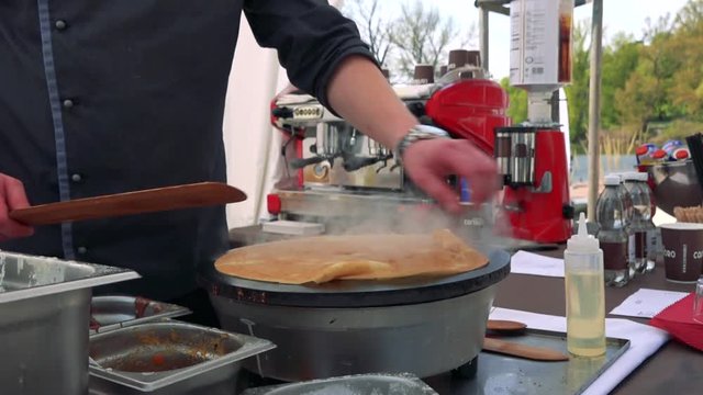Man bakes and turns a pancake on hotplate outside