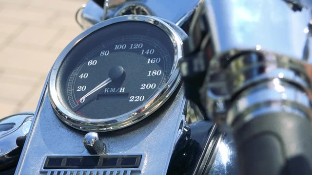 A speedometer, a shiny handlebar in the foreground and out of focus