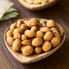 Roasted peanuts in spicy coat, photographed on dark wood with natural light (Selective Focus, Focus one third into the peanuts)