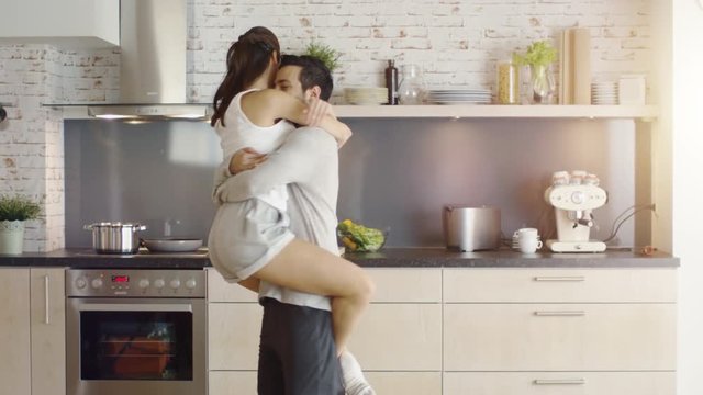 Young Couple Dances in the Kitchen then Girl Flirtatiously Jumps in Man's Arms. Shot on RED Cinema Camera in 4K (UHD).