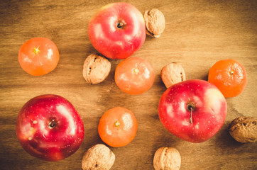 Organic apples, tangerines and walnuts on a wooden background.