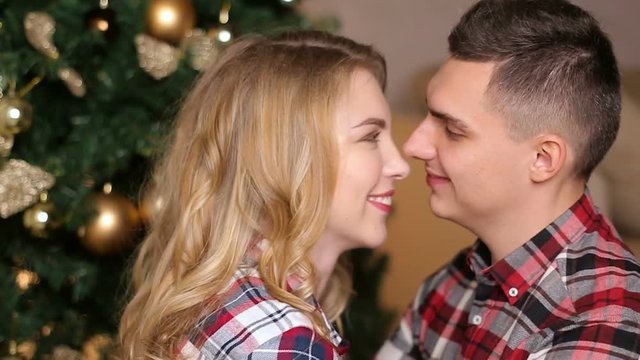 young couple boy and girl in checkered shirts at the Christmas tree in the apartment