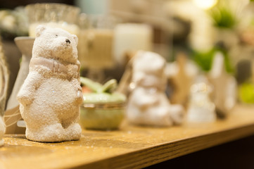 Cute white Christmas teddy bear made of porcelain is on the shelf in the background of other toys