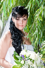 Beautiful bride posing in a park with a wedding bouquet.