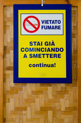 "Vietato Fumare" ("No Smoking") signboard in italian language with the message "Se stai cominciando a smettere continua" ("if you're trying to stop go on"), hanging from a wooden screen