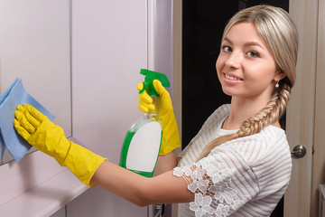 Young lady wiping mirror with blue cloth and special cleaning