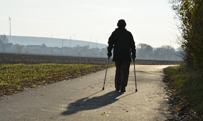 eine frau geht an krücken auf einem feldweg