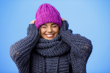 Young beautiful fair-haired girl in knited hat and sweater smiling over blue background. 