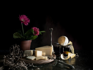still life. Pink gerbera in a pot, lemon, cheese, Dor Blue, knife on wooden table dark background