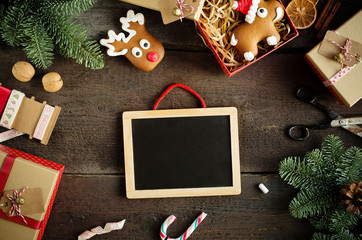 Christmas background with chalkboard, candy cane, decorations, gift boxes, ribbon and ginger bread on wooden board.