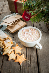 Cup of hot chocolate and gingerbread in the shape of stars on a wooden table, christmas presents and fir-tree branches