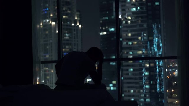 Sad, unhappy man sitting by window during night, 4K 
