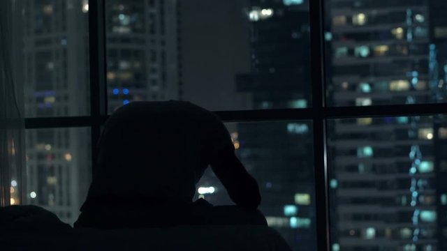 Sad, unhappy man sitting on bed close to the window during night 

