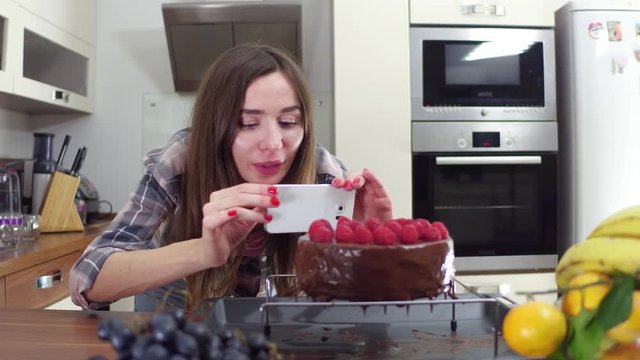 Beautiful brunette girl making pictures of her freshly cooked cake at home. Amateur cooking and social media concept. Steadicam 4K shot