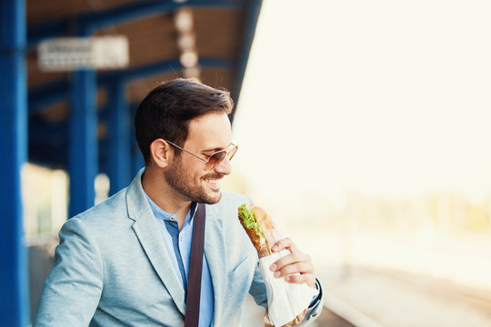 Business person is waiting for train and eating sandwich.