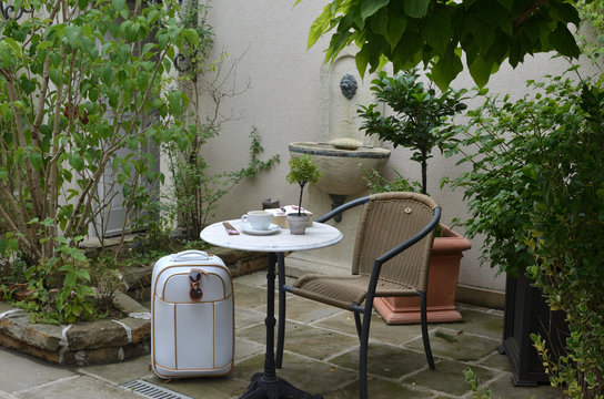 White suitcase near to a table with a fine porcelain cup - in a lush garden