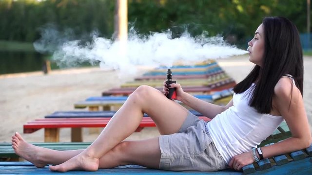 Brunette girl smoking electronic cigarette on the beach