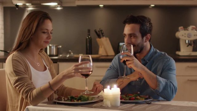 Beautiful Couple Having Candlelight Dinner in the Kitchen. They Eat, Drinl and Talk. In Celebration they Clink Their Glasses.  Shot on RED Cinema Camera in 4K (UHD).