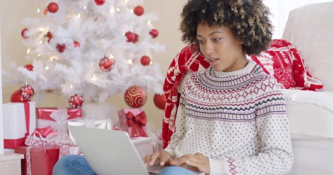Excited young woman making a surprise find on the internet as she surfs the web at Christmas while relaxing in front of the tree