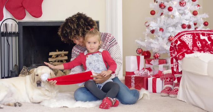 Happy young mother and child seated on white carpet while petting dog on Christmas Day