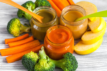 baby mashed with spoon in glass jar on wooden background