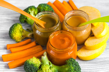 baby mashed with spoon in glass jar on wooden background