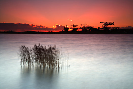 Excavators on abandoned Open Pit Mine by Lake at Sunset