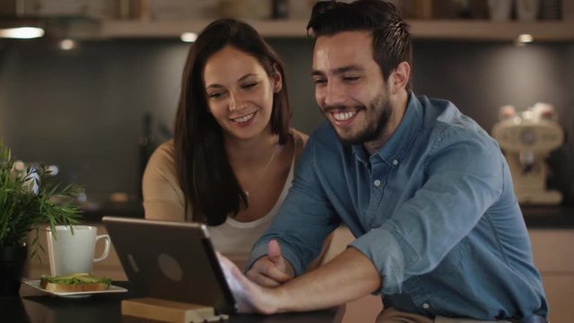 Happy Couple Uses Tablet while Sitting At the Kitchen Table. Shot on RED Cinema Camera in 4K (UHD).