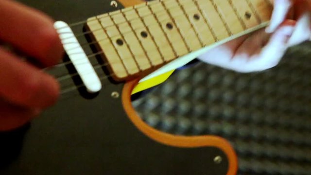 closeup caucasian musician guy runs fingers over guitar strings touches neck at rehearsal in studio