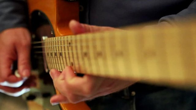 closeup caucasian musician guy runs fingers over guitar neck strings at rehearsal in studio
