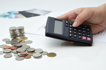 A business man hand using the calculator with coin stacks and financial report on the table 