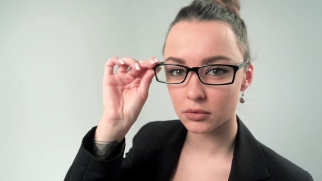  Confident young woman in formalwear adjusting her eyeglasses and looking at camera while standing