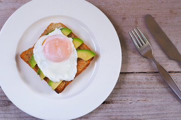 Top view of a breakfast of poached egg and avocado on wholewheat toast on a wooden table.