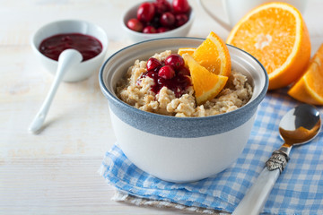  Oat porridge with cranberry sauce and orange in a ceramic bowl for healthy breakfast on a light background. Selective focus.